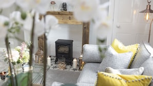 Un salon chaleureux avec une cheminée, un canapé agrémenté de coussins jaunes et une table basse en verre ornée d’objets décoratifs.
