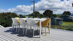 En terrass med ett vitt bord och stolar, omgiven av grönska och en klar himmel.