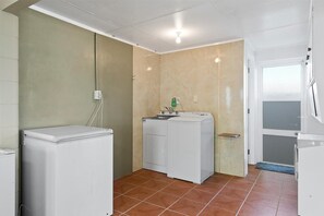 A laundry room with two white washing machines, a sink, and a green bottle on the counter.
