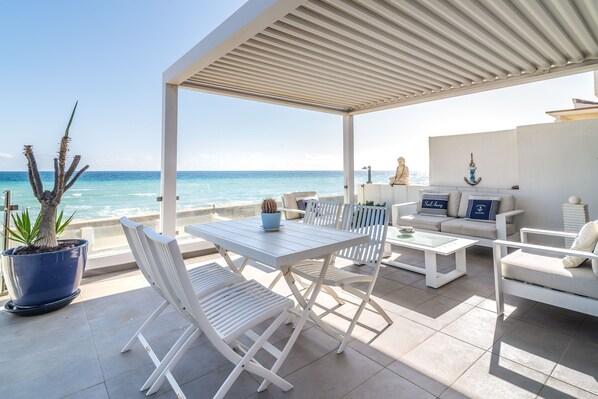 A covered outdoor seating area with a table and chairs, a potted plant, and a view of the ocean. - Holiday Home "Beach-Front Bahía Dorada" with Sea View, Shared Pools and Wi-Fi (Estepona)