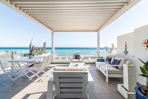 A covered outdoor seating area with a view of the sea, white furniture, and decorative plants. - Holiday Home "Beach-Front Bahía Dorada" with Sea View, Shared Pools and Wi-Fi (Estepona)