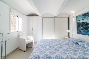A bedroom with a bed, a chair, a nightstand, a lamp, a painting, and a window. - Holiday Home "Beach-Front Bahía Dorada" with Sea View, Shared Pools and Wi-Fi (Estepona)