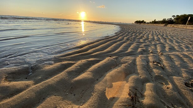 A beach with a clear sky, the sun setting over the horizon, and gentle waves lapping at the shore. - Villa pool & SPA on the Arcachon basin (Lanton)