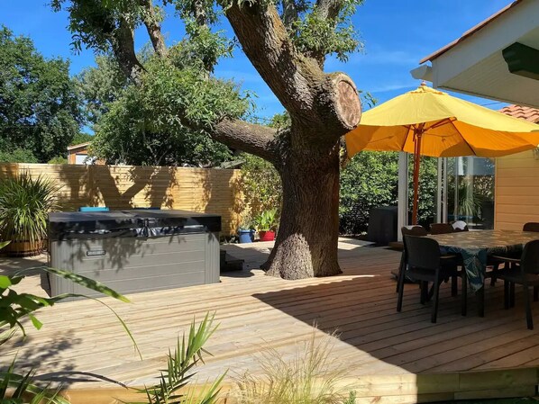 A wooden deck with a hot tub, outdoor furniture, and a yellow umbrella. - Villa with Pool & Spa on the Arcachon Bay (Lanton)