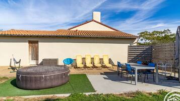Een huis met een pannendak, een terras met een hottub, buiten zitplaatsen en een omheinde tuin.