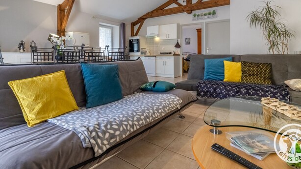 Ein modernes Wohnzimmer mit einer Couch, einem Glastisch und einer Küche im Hintergrund.