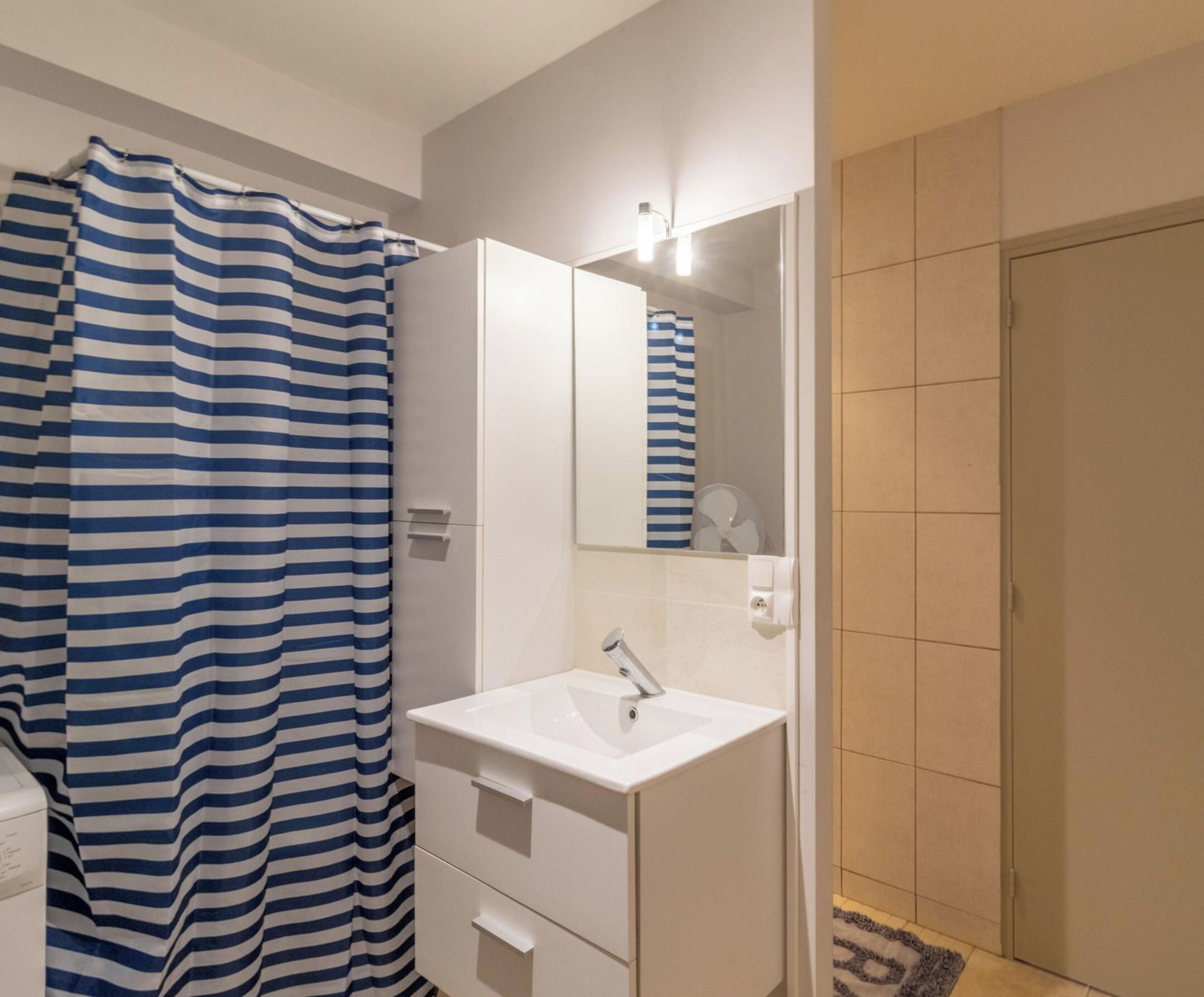 Ein Badezimmer mit einem weißen Waschbecken, einem Spiegel und einem gestreiften Duschvorhang.
