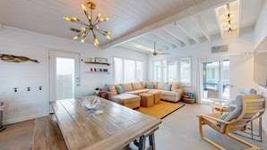 A spacious living room with a wooden table, a sofa set, and a unique ceiling light fixture. - Home in Downtown with Shared Pool, Near Beach, Golf Cart Access (Port Aransas)