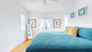 A bedroom with a large bed, white walls, and a view through a glass door. - Home in Downtown with Shared Pool, Near Beach, Golf Cart Access (Port Aransas)