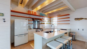 A kitchen with a white refrigerator, stove, and sink, wooden shelves above the counter, and a sign that reads "BIG CHILL". - Home in Downtown with Shared Pool, Near Beach, Golf Cart Access (Port Aransas)