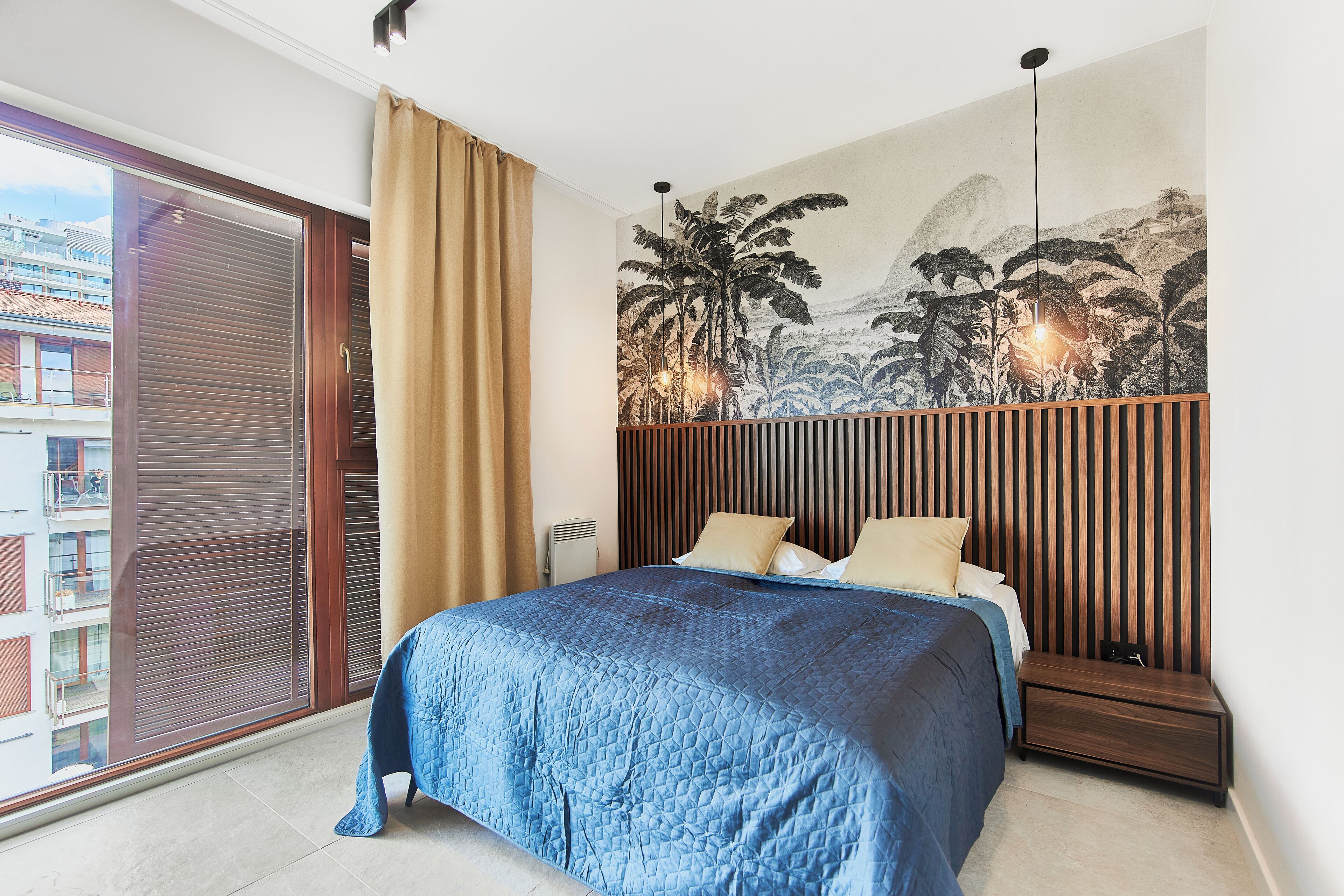 A bedroom with a large bed, a nightstand, a wall mural, and a sliding door to a balcony.
