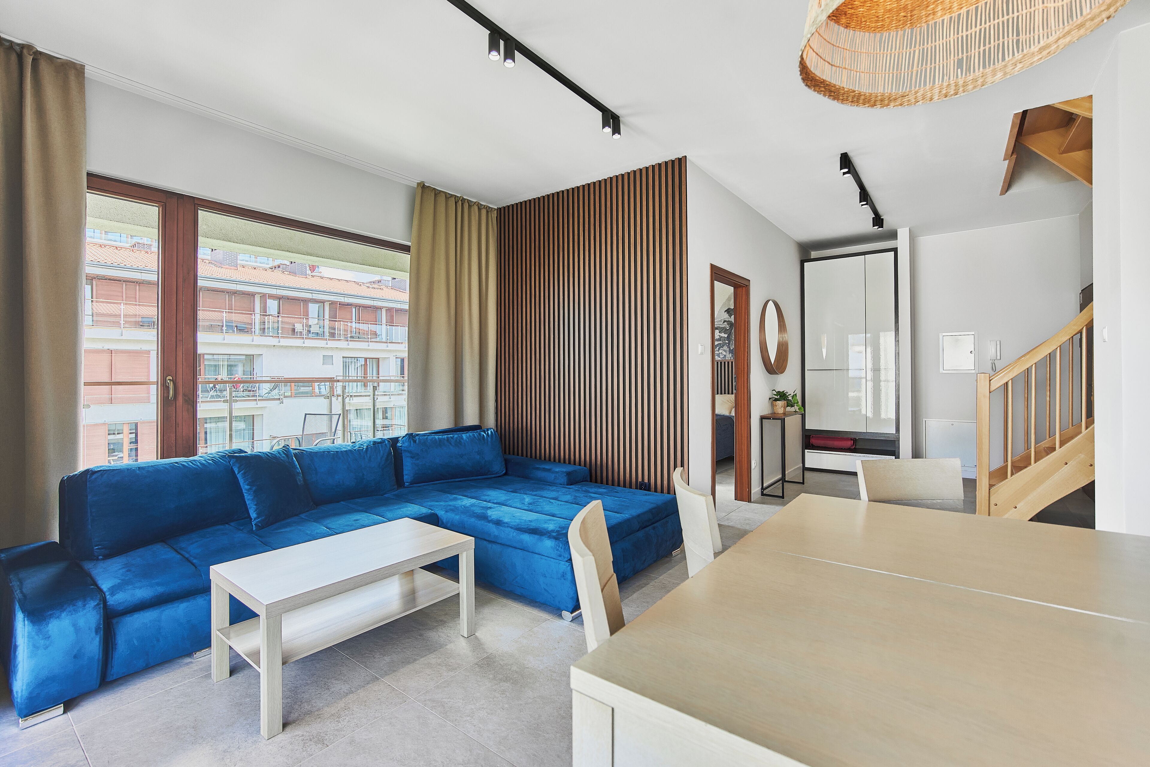 A modern living room with a sectional sofa, a dining table, and a view of the cityscape through large windows.