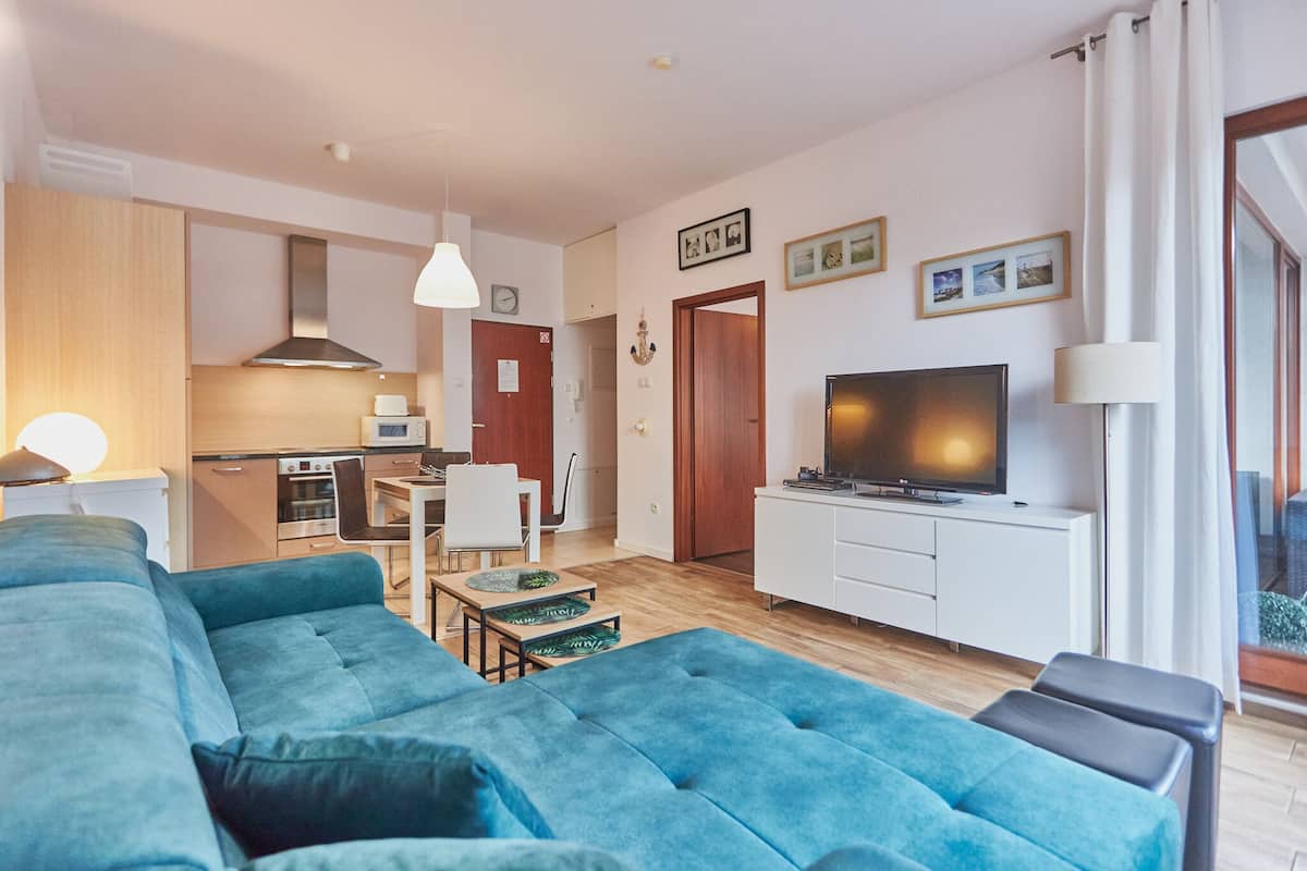 Ett modernt vardagsrum med en blå soffa, en tv och en matplats med ett bord och stolar.