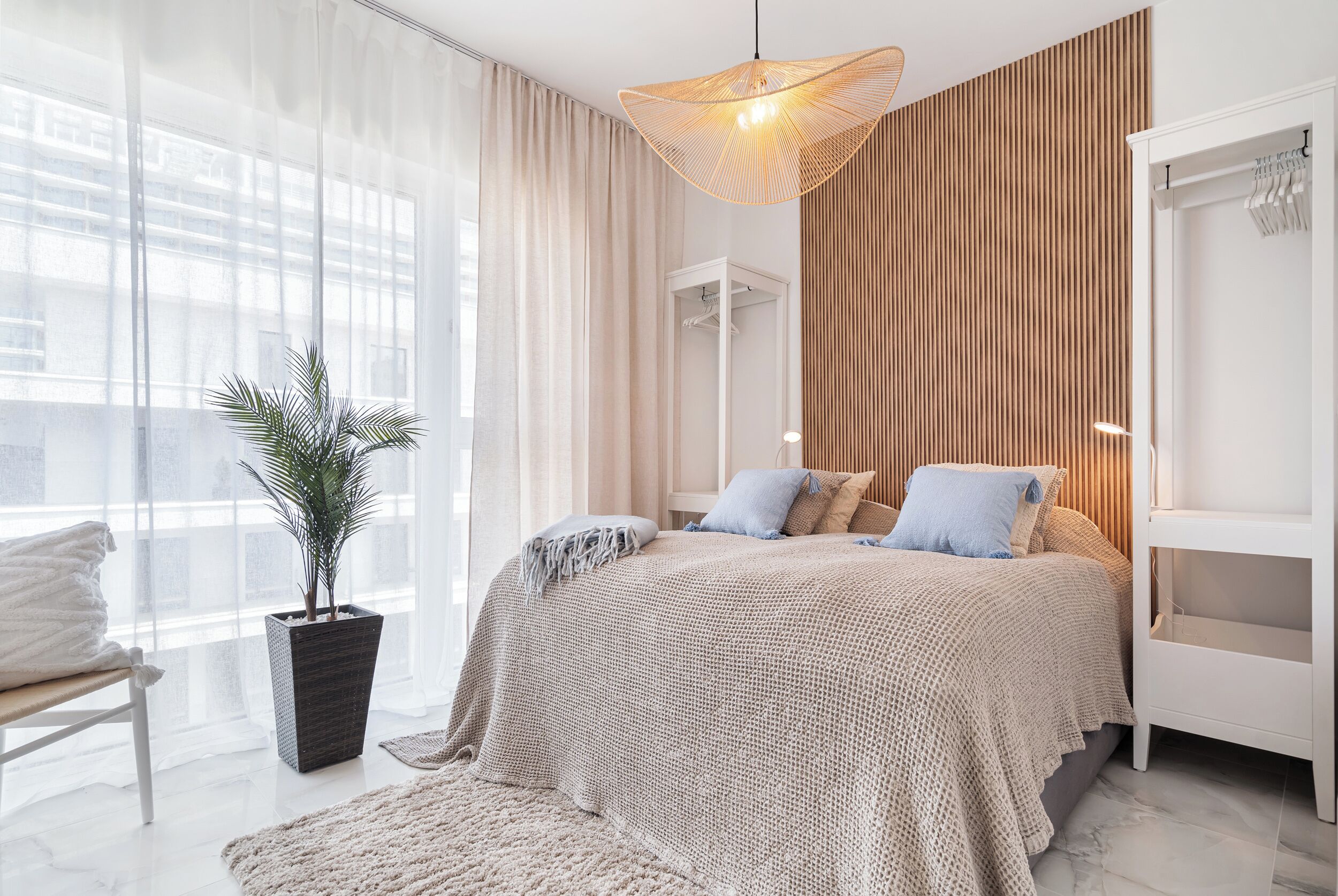 A modern bedroom with a large bed, a potted plant, and a wardrobe.