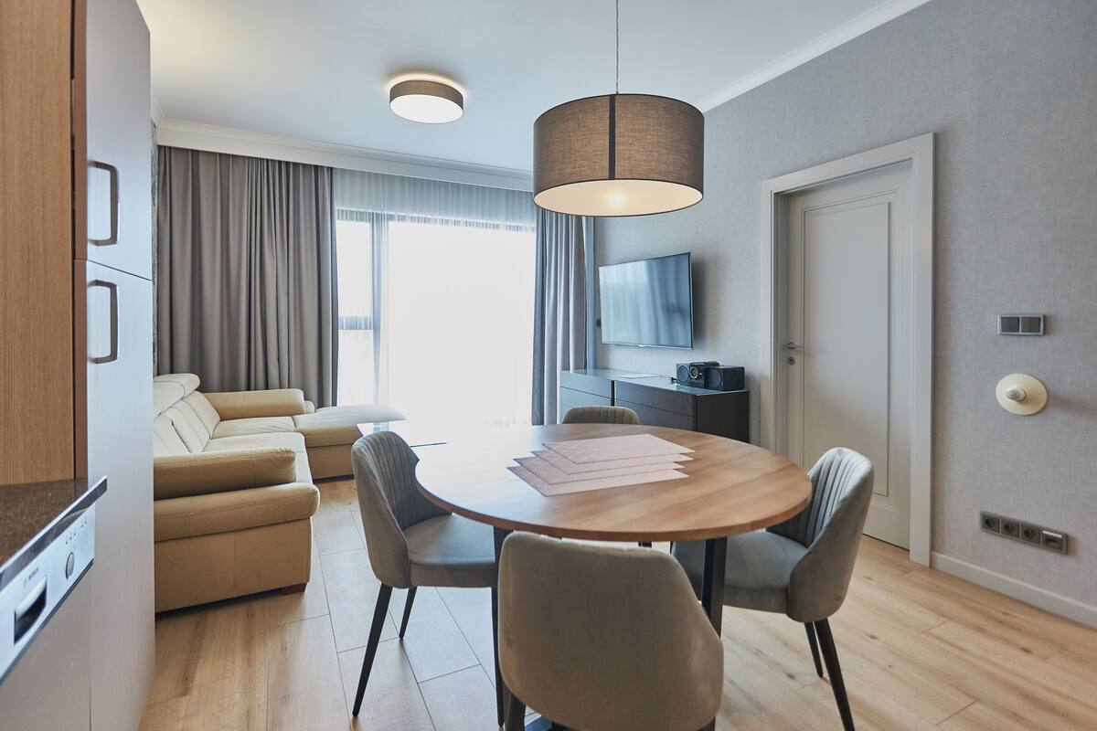 Ett modernt vardagsrum med ett runt träbord, en beige soffa och en tv som är monterad på väggen.
