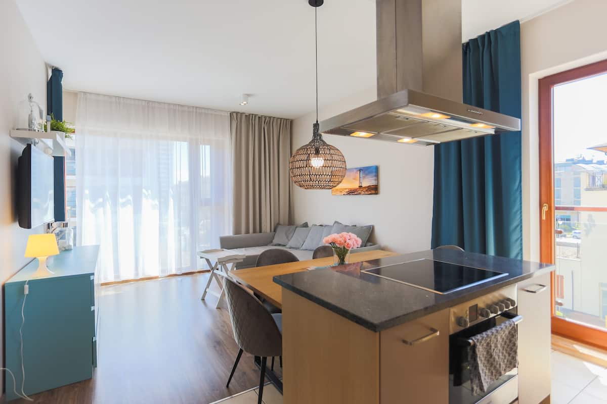 Ett modernt kök med en köksö i mitten, en matplats med en soffa och ett stort fönster med gardiner.