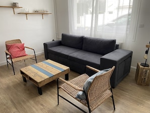 A living room with a dark grey sofa, two wicker chairs, a wooden coffee table, and a small shelf with glasses. - Very pleasant house close to the beach and shops (Le Pouliguen)