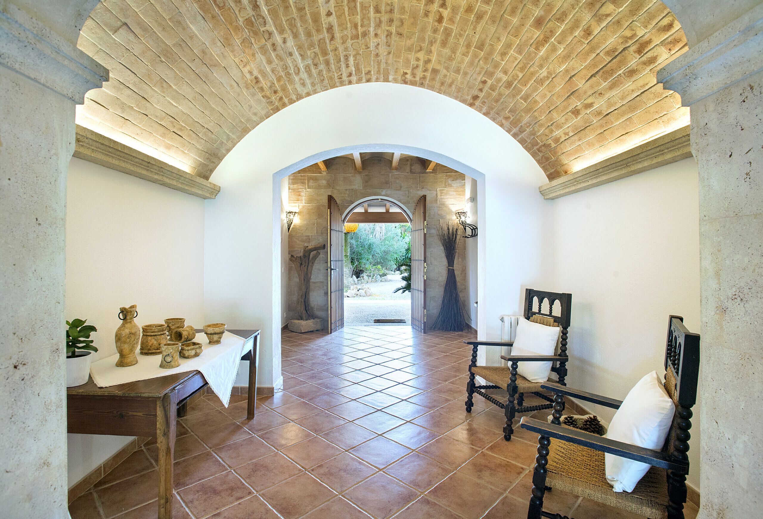 Una habitación con suelo de baldosas, una mesa con cerámica, una silla y un arco de entrada al exterior.