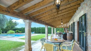 A covered patio with a pool, wicker chairs, and a table with fruit and drinks.