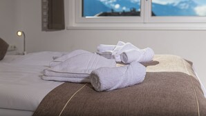 A neatly made bed with white and brown linens, a window with a mountain view, and a bedside lamp.