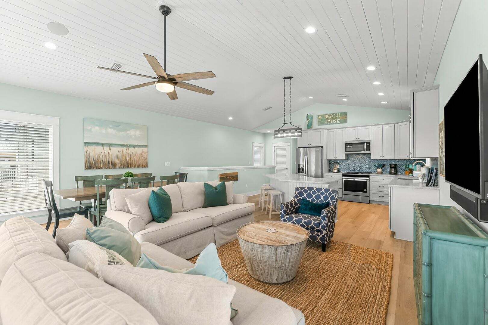 A spacious living room with a sofa, a patterned armchair, a coffee table, and a dining area with chairs and a table.