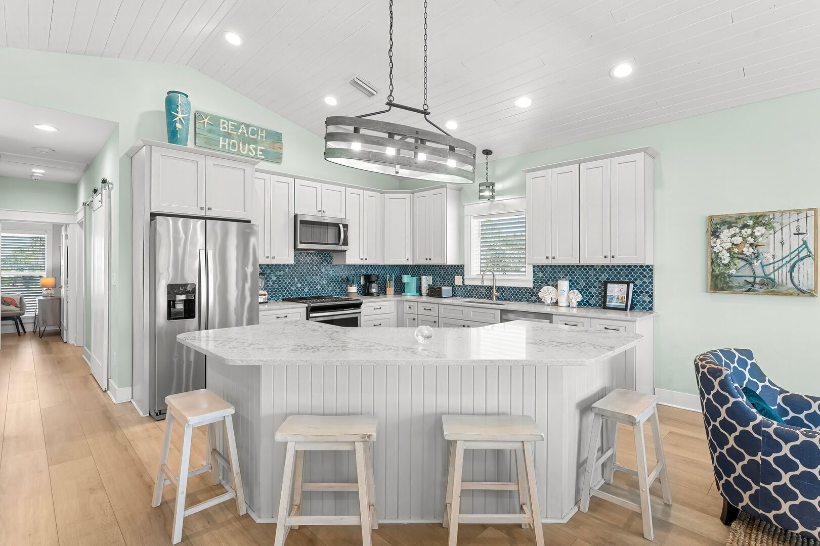 Una cocina moderna con una isla central, armarios blancos y una lámpara colgante.