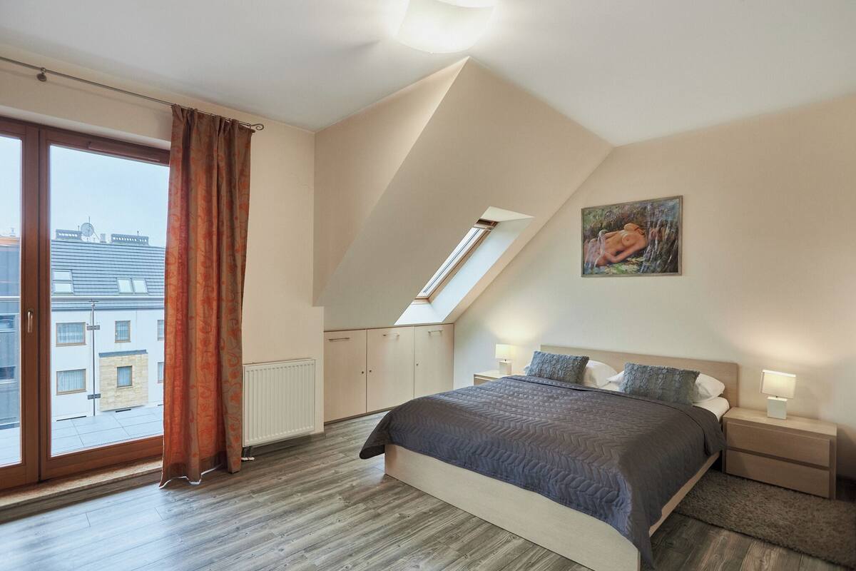 Un dormitorio con una cama grande, un tragaluz, vistas de edificios y un cuadro en la pared.
