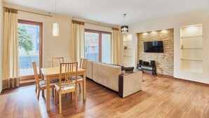 Un amplio salón con una mesa de comedor de madera, sofá y televisor fijado a una pared de piedra.