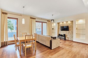 Ein geräumiger Wohnbereich mit Esstisch aus Holz, einer Couch und einem an einer Steinwand befestigten Fernseher.