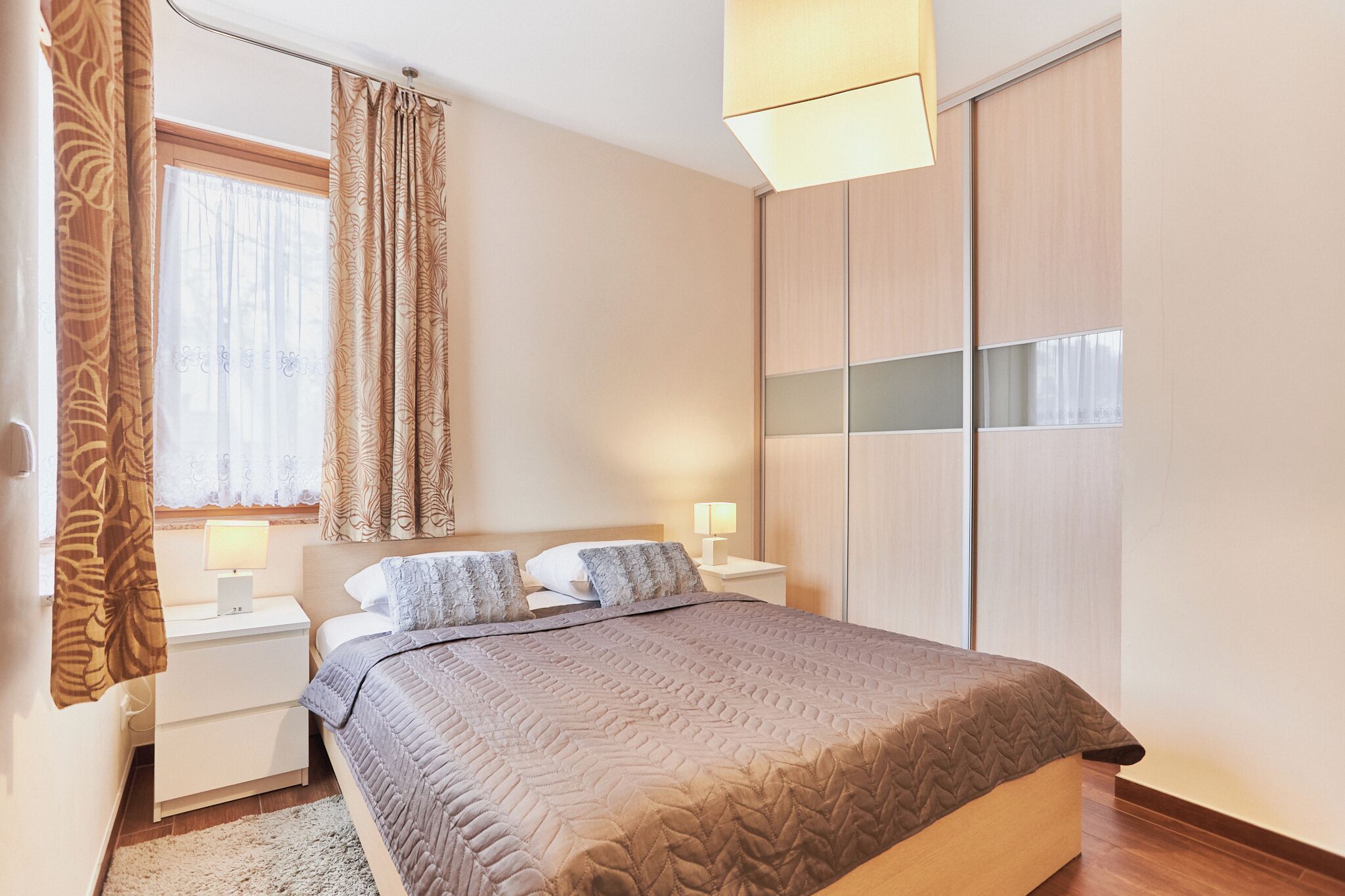 Un dormitorio con cama, mesitas de noche, lámpara, armario y cortinas.