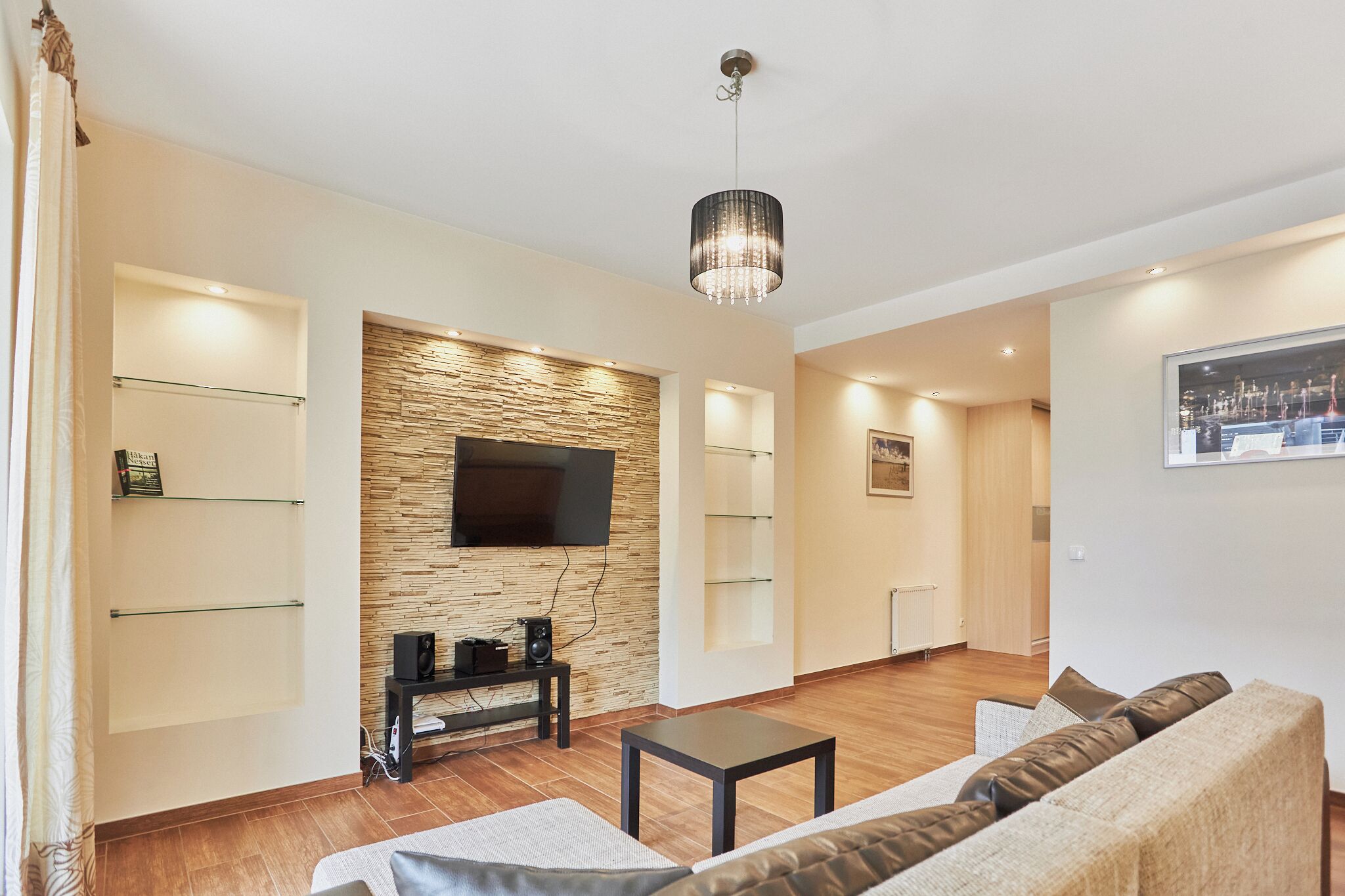 Een moderne woonkamer met een flatscreen televisie, een houten accentmuur, een kroonluchter en een bank.