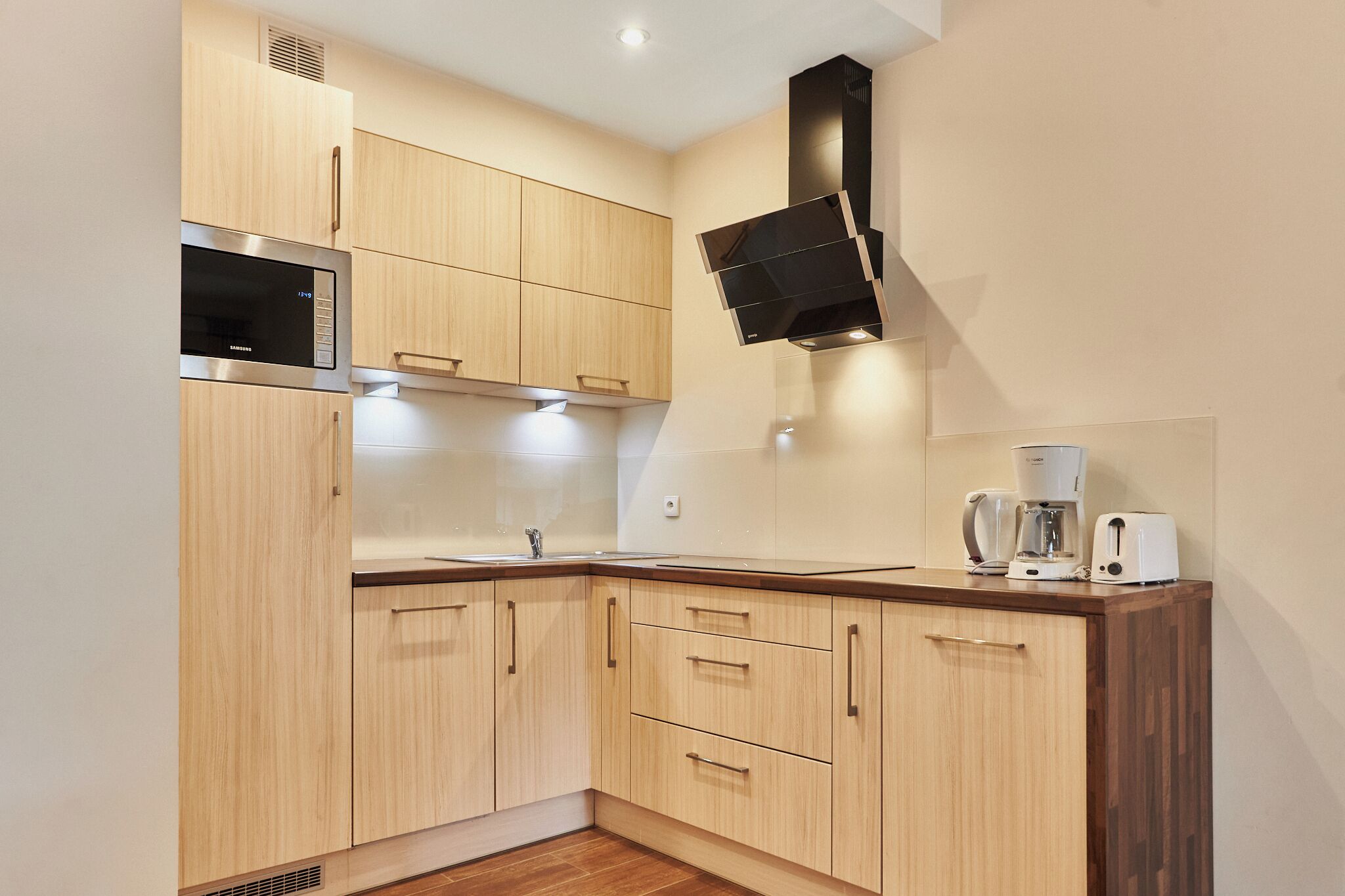 Een moderne keuken met houten kastjes, een roestvrijstalen magnetron, een koffiezetapparaat en een broodrooster.
