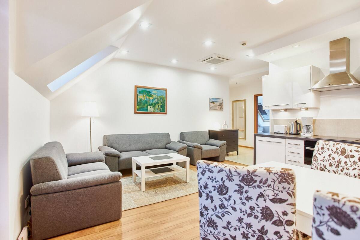 Una sala de estar moderna con un sofá, sillas, una mesa de centro y una cocina con armarios y una estufa.