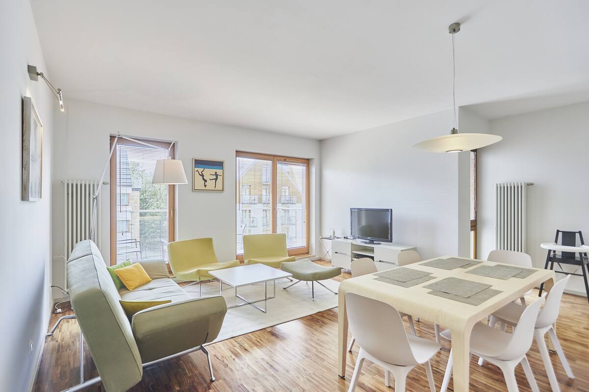 Una sala de estar moderna con comedor, que incluye un sofá, sillas, una mesa y un televisor.