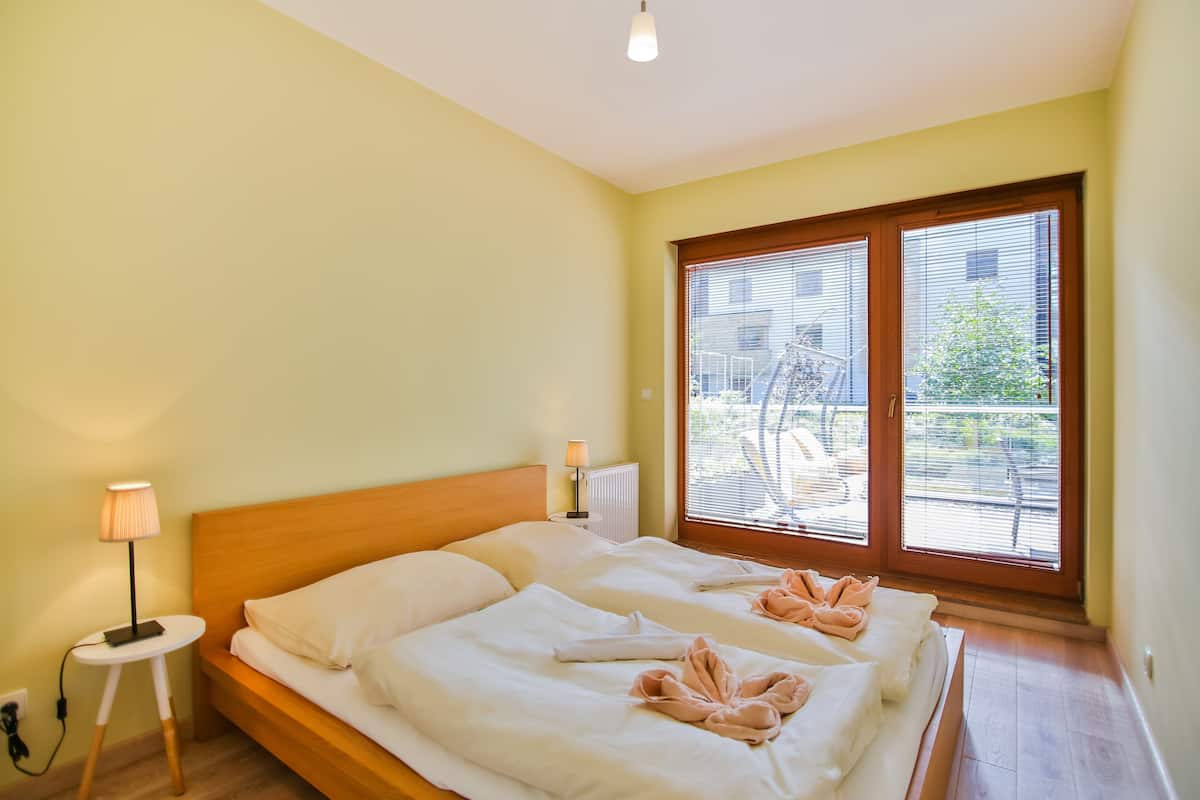 Habitación de hotel con dos camas, una mesita con lámpara y vistas al exterior por un gran ventanal.