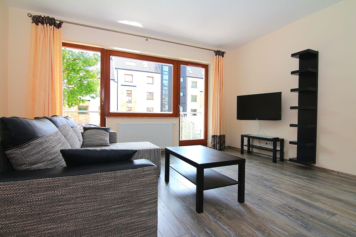 Una sala de estar con un sofá, una mesa de centro, un televisor y una ventana con cortinas.