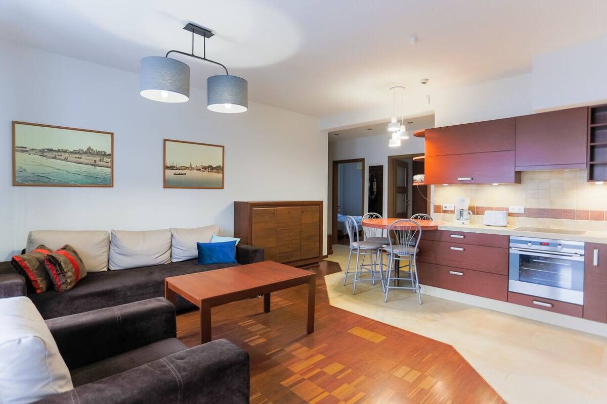 Una sala moderna con sofá, una mesa de centro y una zona de comedor con sillas. Hay una cocina con armarios y una estufa.