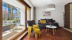 En moderne stue med sofa, sofabord og et stort vindue med udsigt over en have.