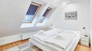 Un dormitorio con techo inclinado, tragaluces, una cama con toallas, una mesita de noche y un cuadro.