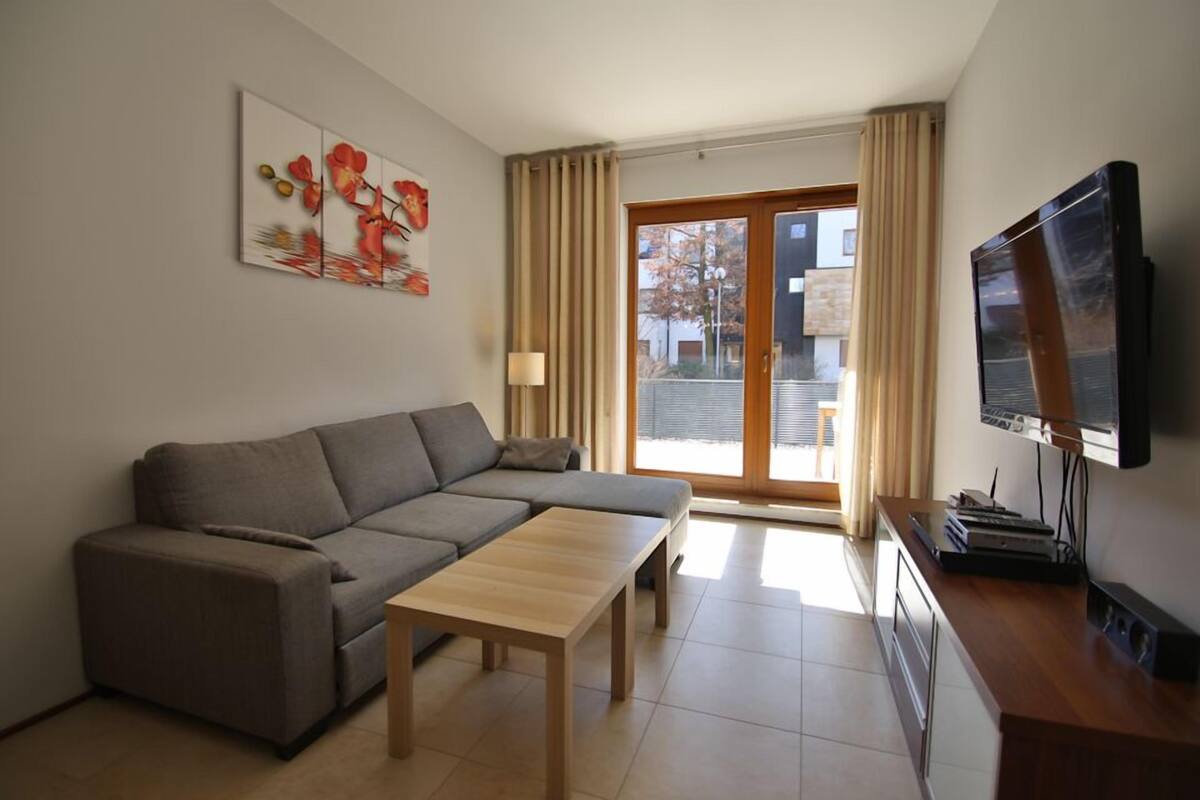Una sala de estar moderna con un sofá gris, una mesa de centro de madera y un televisor de pantalla plana sobre un mueble de madera.