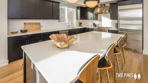 Una cocina moderna con armarios oscuros, una isla grande y un refrigerador de acero inoxidable.
