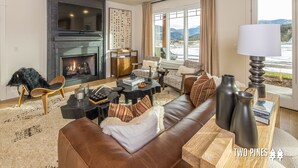 Una sala de estar moderna con chimenea, sofá de cuero y vistas a las montañas a través de amplias ventanas.