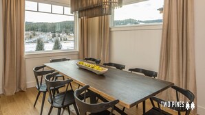 Un comedor con una larga mesa de madera, seis sillas, un cuenco de limones y vistas a un paisaje nevado a través de amplios ventanales.