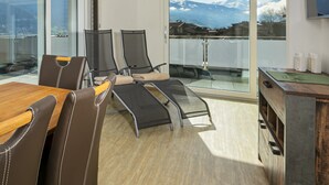 Una habitación moderna con una mesa de madera, sillas de cuero, un sofá y un balcón con vistas a la montaña.