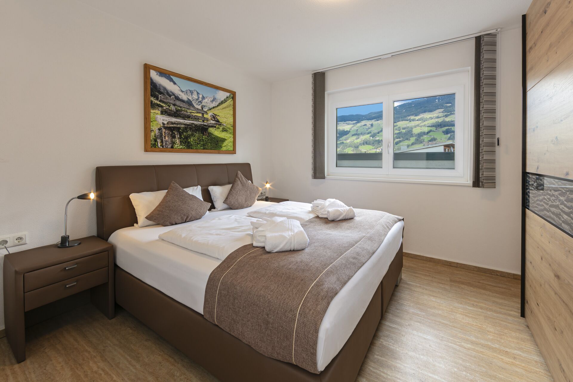 A bedroom with a bed, nightstand, lamp, and a window with a view of a landscape.