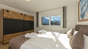 Habitación de hotel con una cama, un armario de madera, un ventanal con vistas a la montaña y un cuadro en la pared.