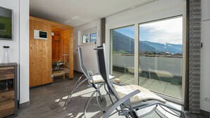 Una habitación moderna con un muro de madera, un vidrio que da a un balcón con vistas a la montaña, y una silla.
