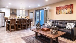 A modern living room with a wooden dining table, a leather sofa, and a large abstract painting on the wall.