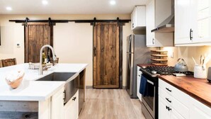A modern kitchen with a central island, white cabinetry, a wooden sliding door, and a stainless steel refrigerator.