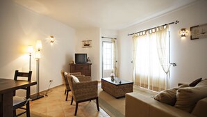 A living room with a dining table, chairs, a sofa, a television, and a window with curtains.